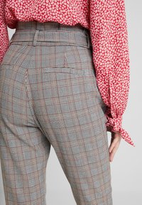 Grå rutiga byxor med röda detaljer, med hög midja och bakfickor, i kombination med en blommig röd blus.