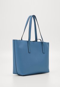 Sininen kassi, joka on valmistettu sileästä synteettisestä materiaalista, suorakulmainen muoto, kaksi pitkää kantohihnaa ja kontrastiväriset mustat ompeleet.