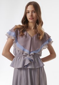 Peplum-top met gelaagde, gerimpelde mouwen in zacht mauve en lichtblauw. Gemaakt van lichte stof, met een elastische tailleband en v-hals.