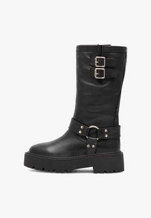 Stivale in pelle nera fino al polpaccio con suola spessa, due fibbie regolabili sulla parte superiore e una fascia decorativa con anello metallico intorno alla caviglia.
