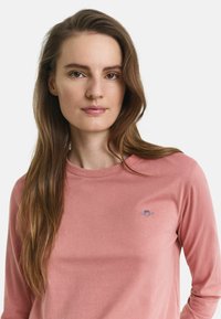 Langärmliges pinkes Shirt aus weichem Stoff, mit kleinem gesticktem Logo auf der Brust, relaxedem Ausschnitt und eng anliegenden Ärmeln.