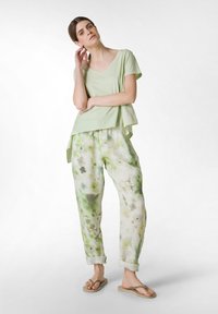 Lichtgroene top met korte mouwen en een gelaagd ontwerp; losse, gestreepte broek in groen en beige; gedragen met eenvoudige slippers.