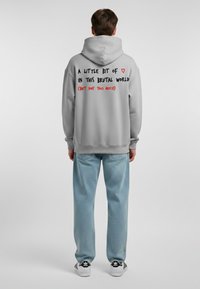 Felpa grigia con un grande e prominente testo grafico nero e rosso sul retro. Abbinata a jeans blu chiaro e sneakers bianco e nere.