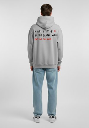Felpa grigia con un grande e prominente testo grafico nero e rosso sul retro. Abbinata a jeans blu chiaro e sneakers bianco e nere.