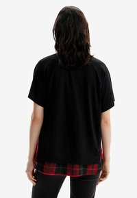 Camisa negra de manga corta con un corte holgado, superpuesta sobre una camisa de cuadros roja y negra. Material de algodón con una textura suave.