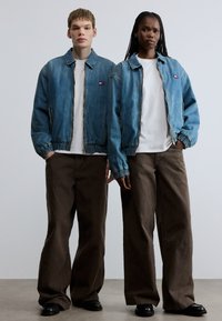 Džínové bomber bundy svetlomodrej farby, biele tričká a hnedé nohavice s širokými nohavicami. Čierne topánky a elastické manžety na bundách. Jednoduchý dizajn, voľný strih.