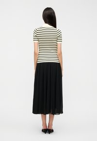 Ριγέ τοπ με κοντά μανίκια σε κρεμ και μαύρο, συνδυασμένο με αέρινη μαύρη midi φούστα. Ομαλή υφή, εφαρμοστό μπούστο και σιλουέτα σε γραμμή Α.