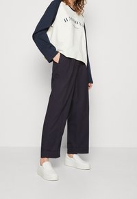 Cremfarbener und marineblauer Langarmoberteil mit dem Text "HARMONY", kombiniert mit weiten Marineblauen Hosen und weißen Slippern. Glattes Material, lockerer Schnitt.