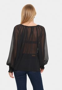 Blusa nera trasparente con maniche lunghe a palloncino e scollatura arricciata. Presenta un design fluido, materiale semi-trasparente e polsini elastici.