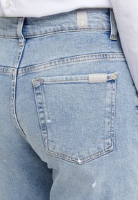 Jasnoniebieskie dżinsy z wyblakłą fakturą, z tylną kieszenią z metką i subtelnymi detalami w stylu distressed.