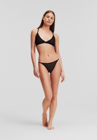 Zwart bikini set met een driehoekige bralette met verstelbare bandjes en een gestructureerd patroon, aangevuld met bijpassende low-rise broekjes.