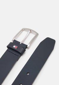 Navy leren riem met een zilveren metalen gesp in rechthoekige vorm, detail van het logo met rode en blauwe accenten, en vijf gaatjes voor aanpassing.