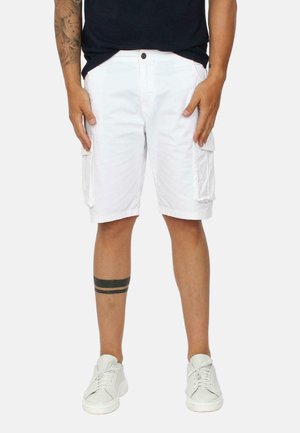 Pantaloni cargo bianchi con due tasche laterali, realizzati in tessuto leggero. Indossati con scarpe da ginnastica bianche e presentano un tatuaggio a strisce nere sopra il ginocchio.