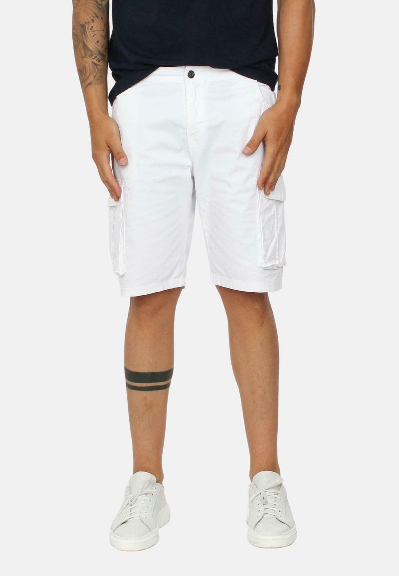 Pantaloni cargo bianchi con due tasche laterali, realizzati in tessuto leggero. Indossati con scarpe da ginnastica bianche e presentano un tatuaggio a strisce nere sopra il ginocchio.
