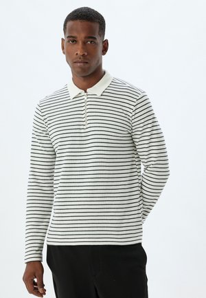 Langærmet polo sweater i creme med fine sorte striber, der har en lynlås i halsen og en klassisk krave, lavet af tekstureret stof.