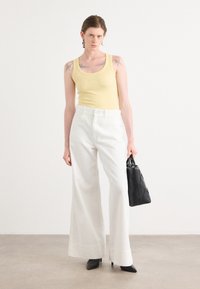 Light yellow fitted tank top, white wide-leg pants, black structured handbag, and pointed black heels. Minimalist design and clean lines.