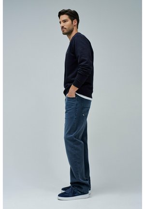 Navy sweatshirt with ribbed cuffs, blue jeans, and navy sneakers. Casual fit, plain design, features side pockets and subtle branding.