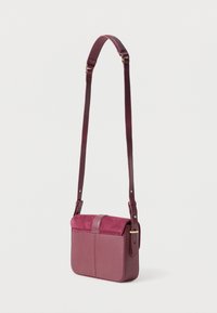 Burgundi színű keresztpántos táska texturált bőr testtel és velúr fedéllel. Hosszú, állítható pántja és arany színű csattja van.