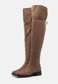 Brązowe kozaki za kolano wykonane z miękkiego zamszu, z płaską podeszwą, zaokrąglonym noskiem i przeszyciami. Posiadają pętelkę z tyłu.