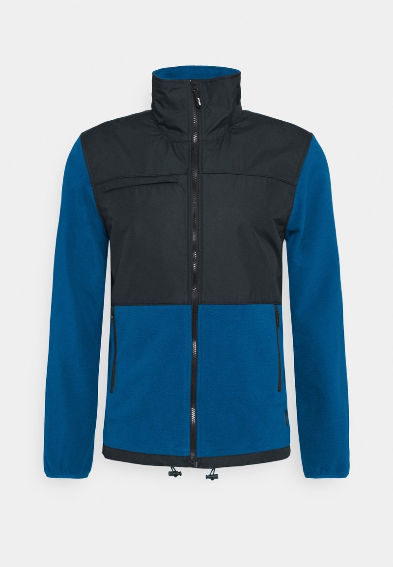 Chaqueta con cremallera azul y negra, con cuello alto, bolsillo en el pecho con cremallera, dos bolsillos laterales y bajo con cordón ajustable. Textura suave.