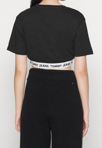 Svart kort t-shirt med en vit elastisk midjeresår med texten "TOMMY JEANS". Korta ärmar och slät bomullstextur.