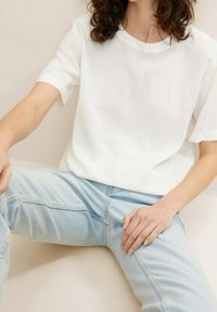 Bílá tričko s krátkým rukávem a kulatým výstřihem, spárované se světle modrými džíny. Hladká tkanina s uvolněným střihem a jednoduchým designem.