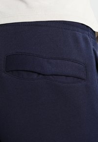 Los pantalones de chándal de felpa en color azul marino cuentan con un bolsillo trasero con una solapa cosida, diseñados para brindar comodidad y practicidad.
