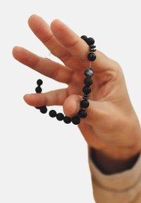 Pulsera de cuentas negras sostenida en una mano, que presenta cuentas redondas de diversos tamaños con un acabado mate, intercaladas con separadores metálicos.