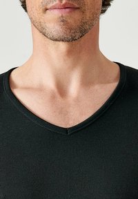 Zwarte V-hals t-shirt gemaakt van een geribde stof, met een aansluitend ontwerp. De halslijn is subtiel gebogen met minimale stikdetails.