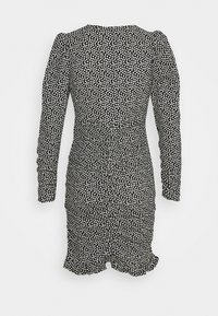 Robe noire à manches longues, présentant un motif à pois blancs, des détails froncés sur les côtés et un ourlet à volants.