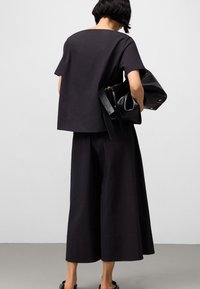 Czarny, teksturowany top i spodnie z szerokimi nogawkami są zestawione z dużą czarną torbą. Strój charakteryzuje się minimalistycznym wzornictwem i luźnym krojem.