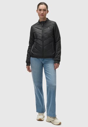 Veste matelassée noire avec un col montant et des manches grises, associée à un jean droit bleu clair et des baskets beiges.