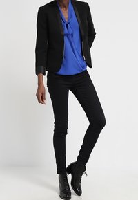 Svart figursydd kavaj med satängdetaljer, matchad med en blå blus med rosett. Svarta skinny jeans och svarta snörningstövlar.