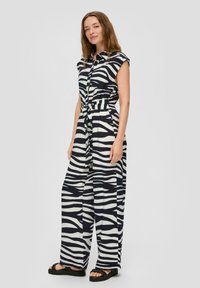 Combinaison à motif zèbre en noir et blanc. Caractéristiques : manches courtes, devant boutonné et taille nouée. Tissu fluide et léger avec des jambes larges.
