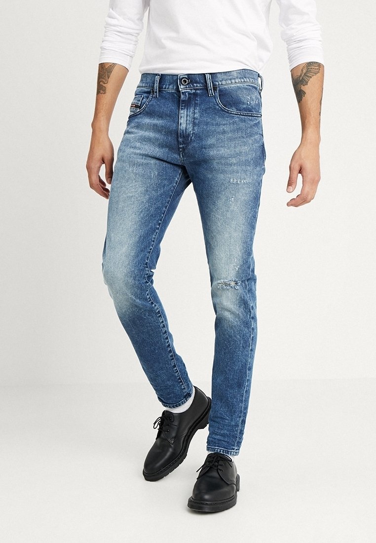 Light blue denim jeans with distressed details, slim fit design, five-pocket style, and a button closure. Worn with black shoes.
