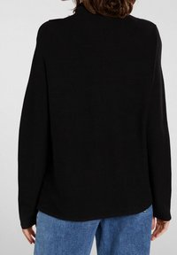 Svart tröja med hög hals, långa ärmar och en avslappnad passform. Materialet verkar mjukt med en slät yta. Inga synliga mönster.