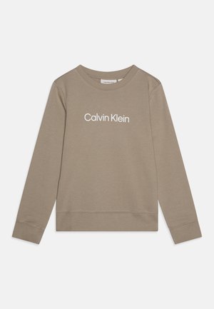 Beige langærmet crewneck-sweatshirt med hvid "Calvin Klein" tekst centreret på brystet, liggende fladt på en hvid baggrund.