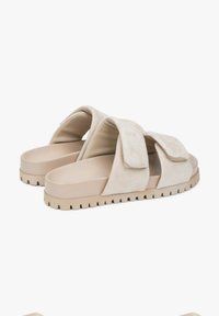 Beige slide sandals with two wide, overlapping straps made of soft suede, featuring a textured rubber sole with a zigzag pattern.