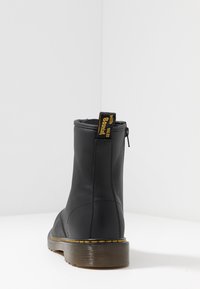 Bottine noire avec un matériau lisse, bout rond, fermeture éclair sur le côté et couture jaune accentuant la semelle. Dispose d'une languette à l'arrière.