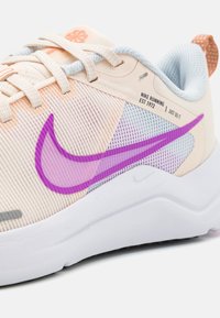 Scarpa da corsa Nike con colori beige e pastello soft, caratterizzata da uno swoosh viola, tomaia in mesh testurizzato e suola bianca con accenti a motivi.