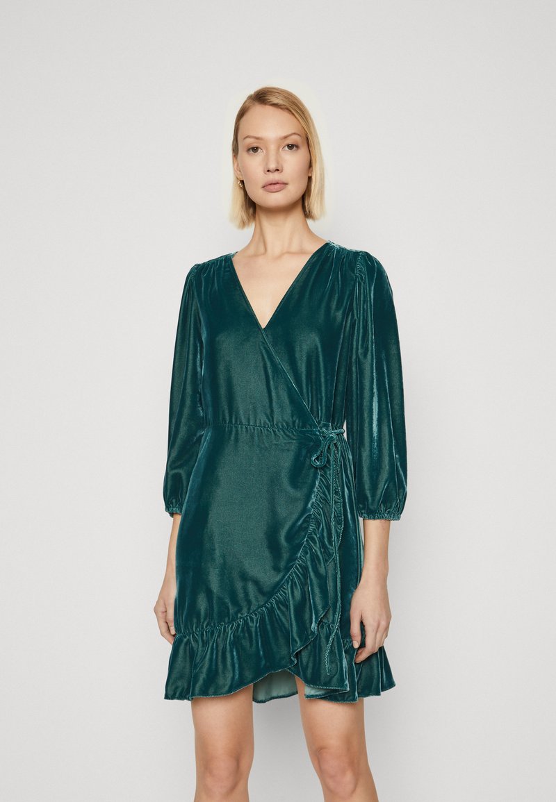 Türkis sametist mähkmekleid V-kaelusega, kolmeveerandi varrukatega ja volangiga alläänega. Omab tooli detaili vööl ja siledat tekstuuri.
