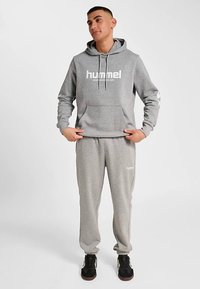 Grå huvtröja och matchande mjukisbyxor av mjukt material, med framficka och vit logotyp. Texturerat tyg med ribbade muddar.