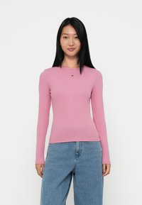 Long-sleeve pink ribbed top with a round neckline and a small logo accent. Paired with loose-fitting light blue denim jeans.