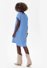 Jasnoniebieska, krótko rękawowa sukienka z miękkiego materiału, z okrągłym dekoltem, bocznymi rozcięciami i małym metalowym akcentem z tyłu.