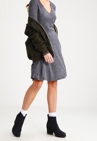 Dzianinowa szara sukienka z dekoltem w serek, połączona z oliwkową kurtką bombką. Czarne botki za kostkę i białe skarpetki dopełniają stylizację.