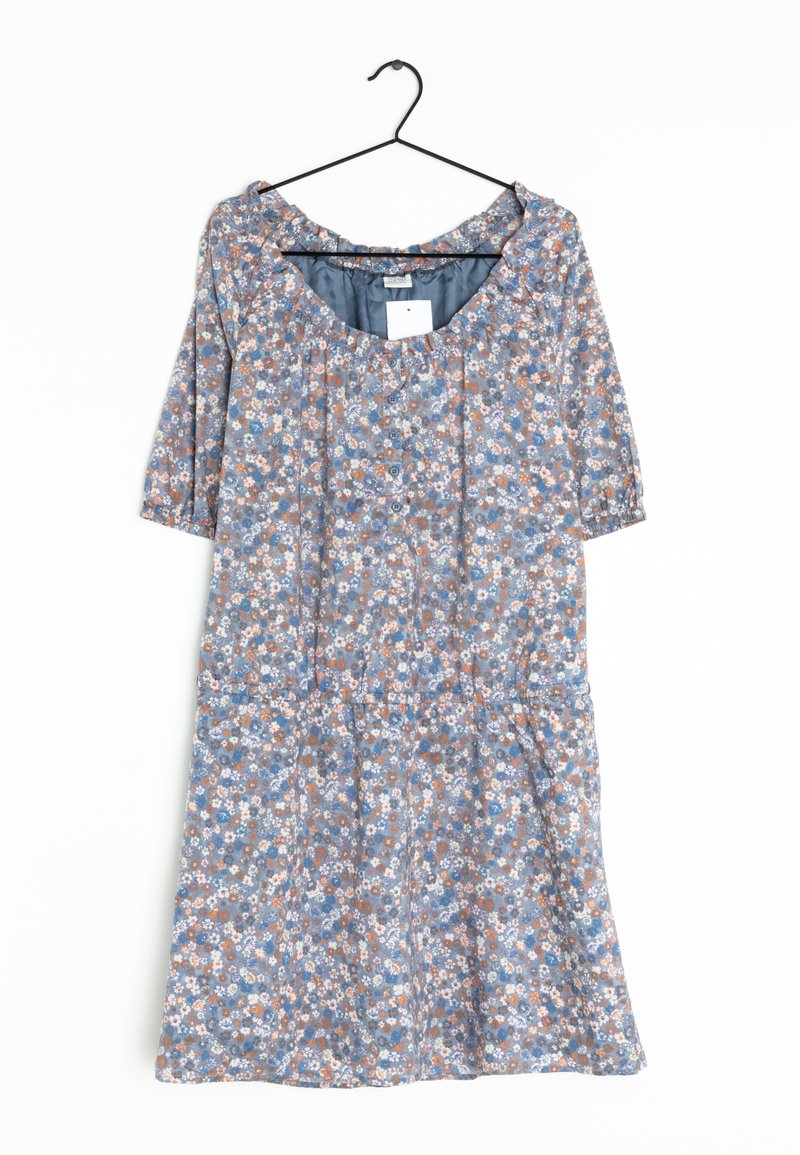 Robe fleurie bleue avec manches bouffantes et boutons sur le devant, suspendue sur un cintre noir contre un fond blanc.