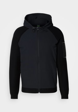 Schwarze Kapuzenjacke. Sie verfügt über einen Reißverschluss vorne, strukturierte Ärmel und einen glatten Körper. Enthält eine aufgesetzte Tasche am linken Arm.