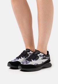 Chaussures de sport noires et argentées avec une tige texturée, présentant un design à motifs, des lacets noirs et une semelle rembourrée.