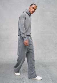 Grijze sweatshirt met een capuchon, gecombineerd met bijpassende losse sweatpants. Beide hebben een zachte textuur en eenvoudig ontwerp, aangevuld met witte sneakers.