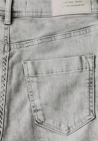 Vaaleanharmaata farkkukangasta, jossa on takatasku, jossa on ompeluyksityiskohtia, tasainen muotoilu ja etiketti, jossa lukee "Street One - Denim".
